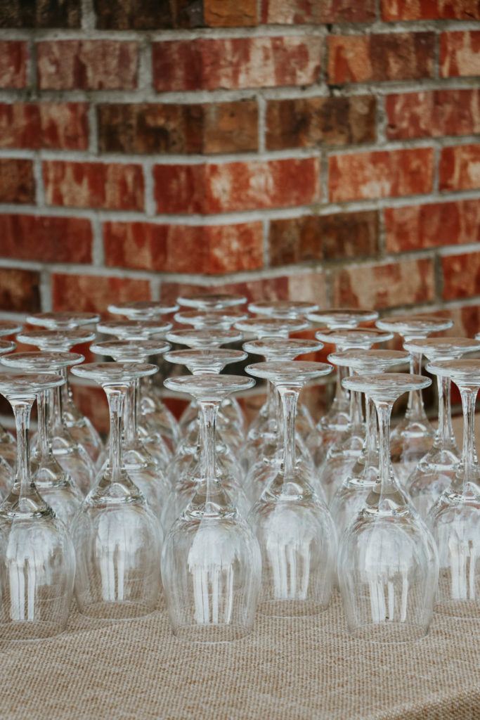 Backyard Rehearsal Dinner Party Tip: Cater the meal! Leave the food to the pros. Eliminate the stress of cooking for a large group by hiring caterers to prepare and serve the meal for you. This will give you more time to spend time with your guests, which is what occasions like this are all about! / theanastasiaco.com / Wine glasses and brick wall